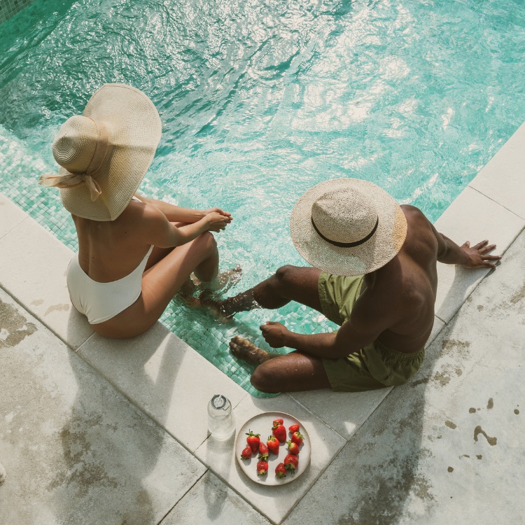 Two residents sitting at the edge of the pool in the afternoon sun, sharing a plate of strawberries