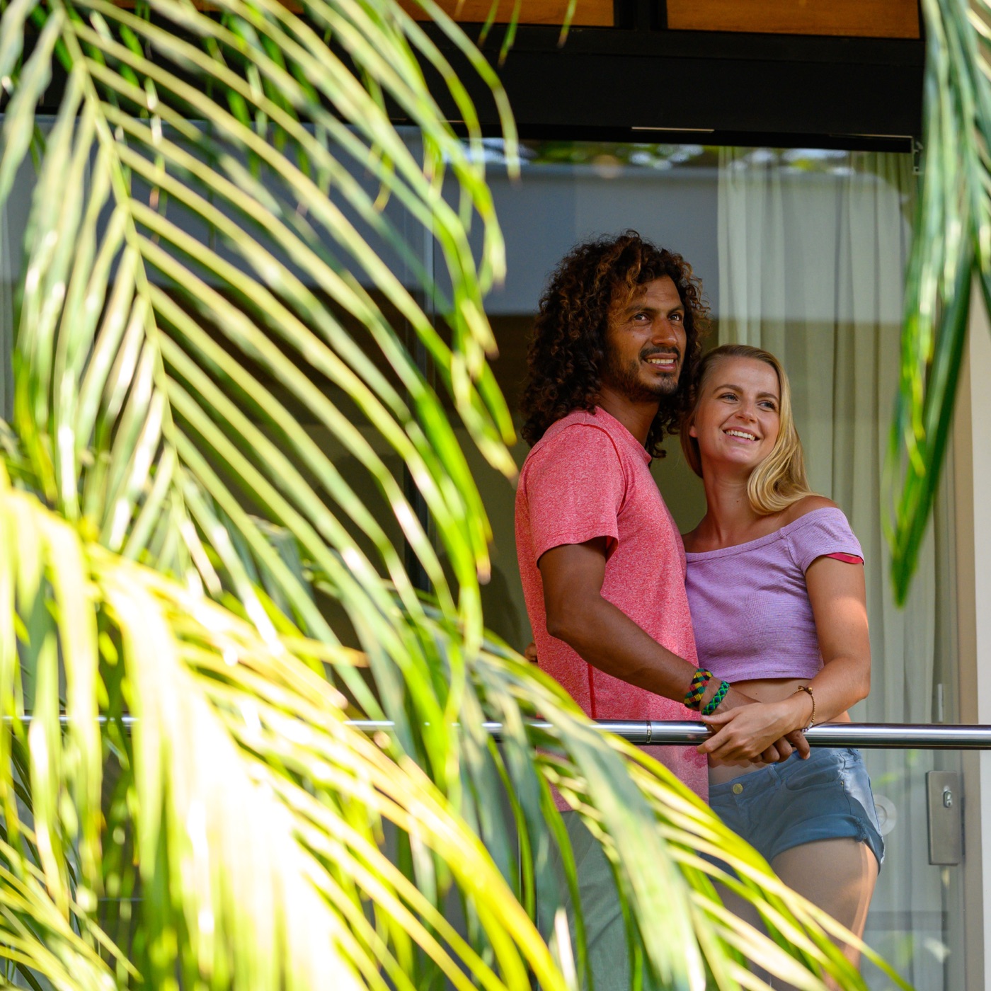 A couple standing together on their balcony at golden hour, framed by palm fronds