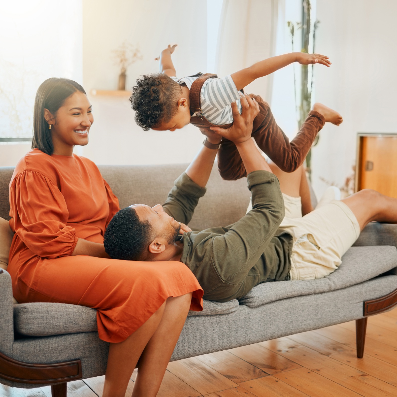 A young family playing together on the sofa of a bright, sunlit living room