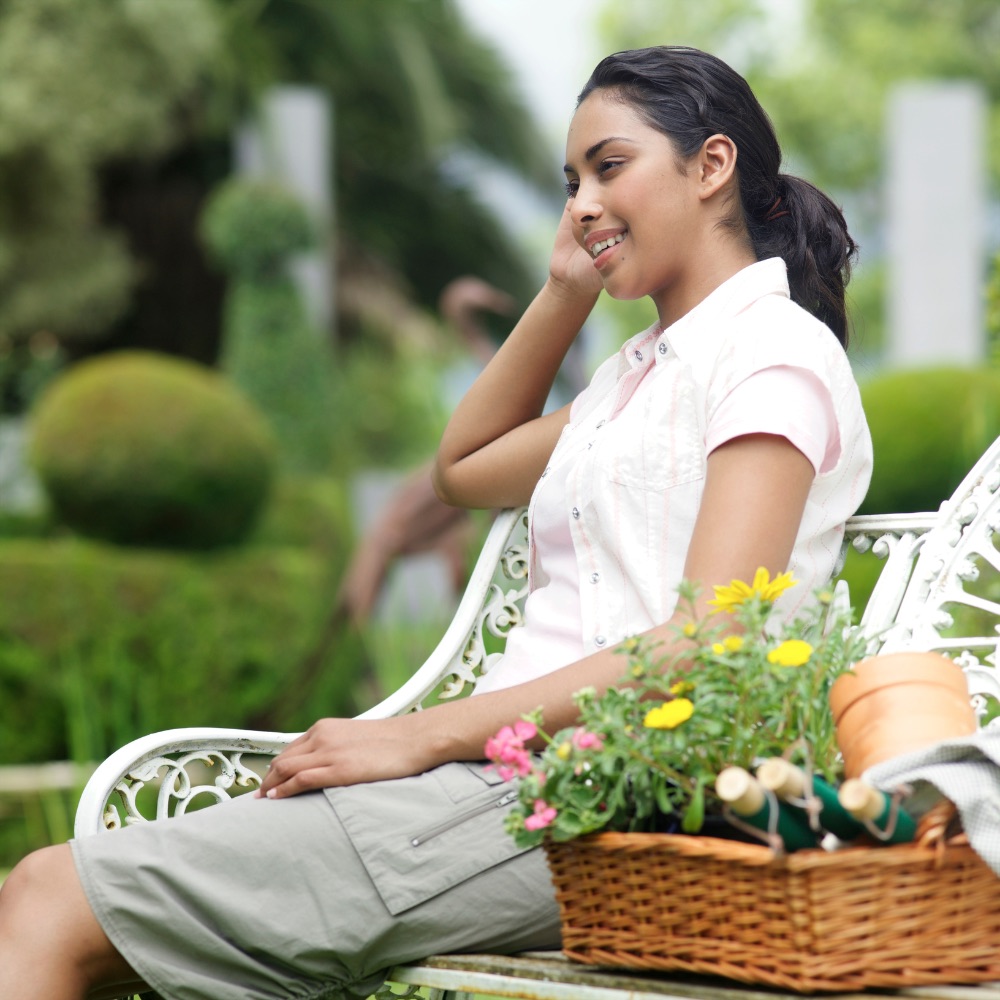 A resident sitting on a bench in a professionally maintained garden, a basket of flowers beside her
